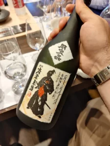 Bouteille de Shochu tenue par une personne, avec une étiquette illustrée représentant un design japonais traditionnel